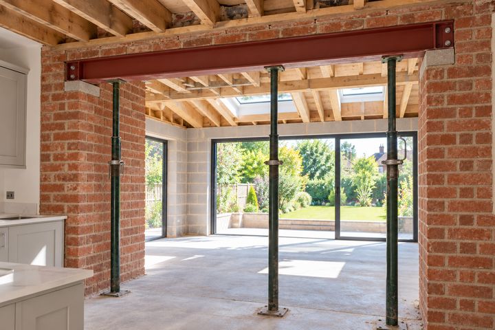 A steel beam on padstones above an opening, supported by props, with bright daylight beyond